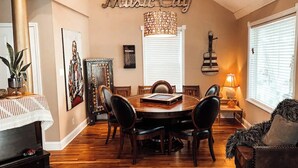 A dining room with a wooden table, chairs, a piano, and a chandelier.
