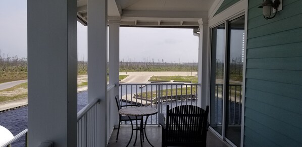 A balcony with a view of a road and water, featuring a table and two chairs.