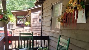 Une véranda en bois avec deux fauteuils à bascule, une petite table et un panier rempli de plantes.