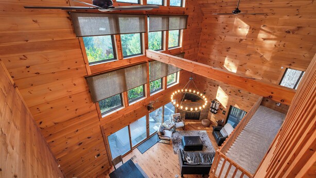 Amplia habitación estilo loft con ventanas grandes, ventilador de techo y un rincón de descanso con chimenea.