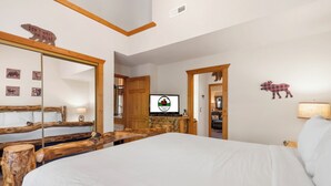 Ein Schlafzimmer mit einem großen Bett, einem Holz-Kopfteil, einem Fernseher und einem Spiegel.