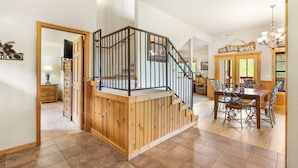 Eine Holztreppe mit Metallgeländer führt zu einer zweiten Etage. Im oberen Bereich ist ein Essbereich mit Holztisch und Stühlen zu sehen.