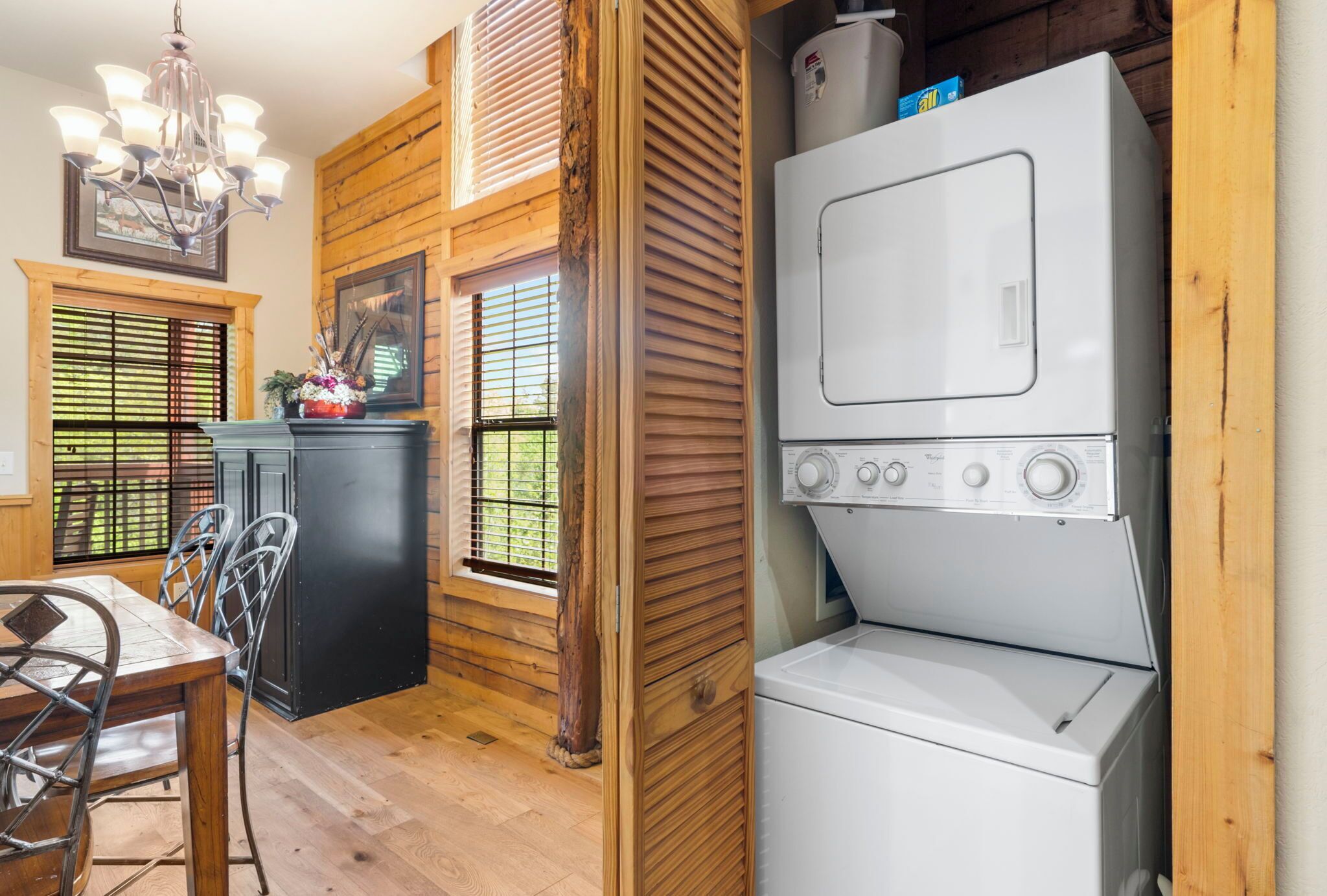 A kitchen with wooden walls, a dining table with chairs, a built-in washer and dryer, and a chandelier.