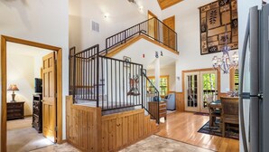 Un amplio espacio habitable con una escalera de madera, una mesa de comedor y un candelabro.