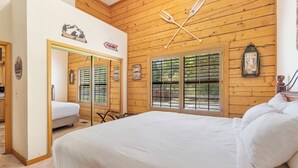 Un dormitorio con techo de madera, cama con ropa de cama blanca, un espejo y una ventana con persianas.