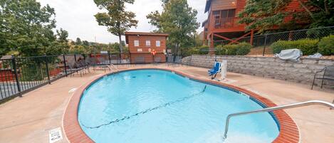 A swimming pool with a brick border, surrounded by lounge chairs and a fence.