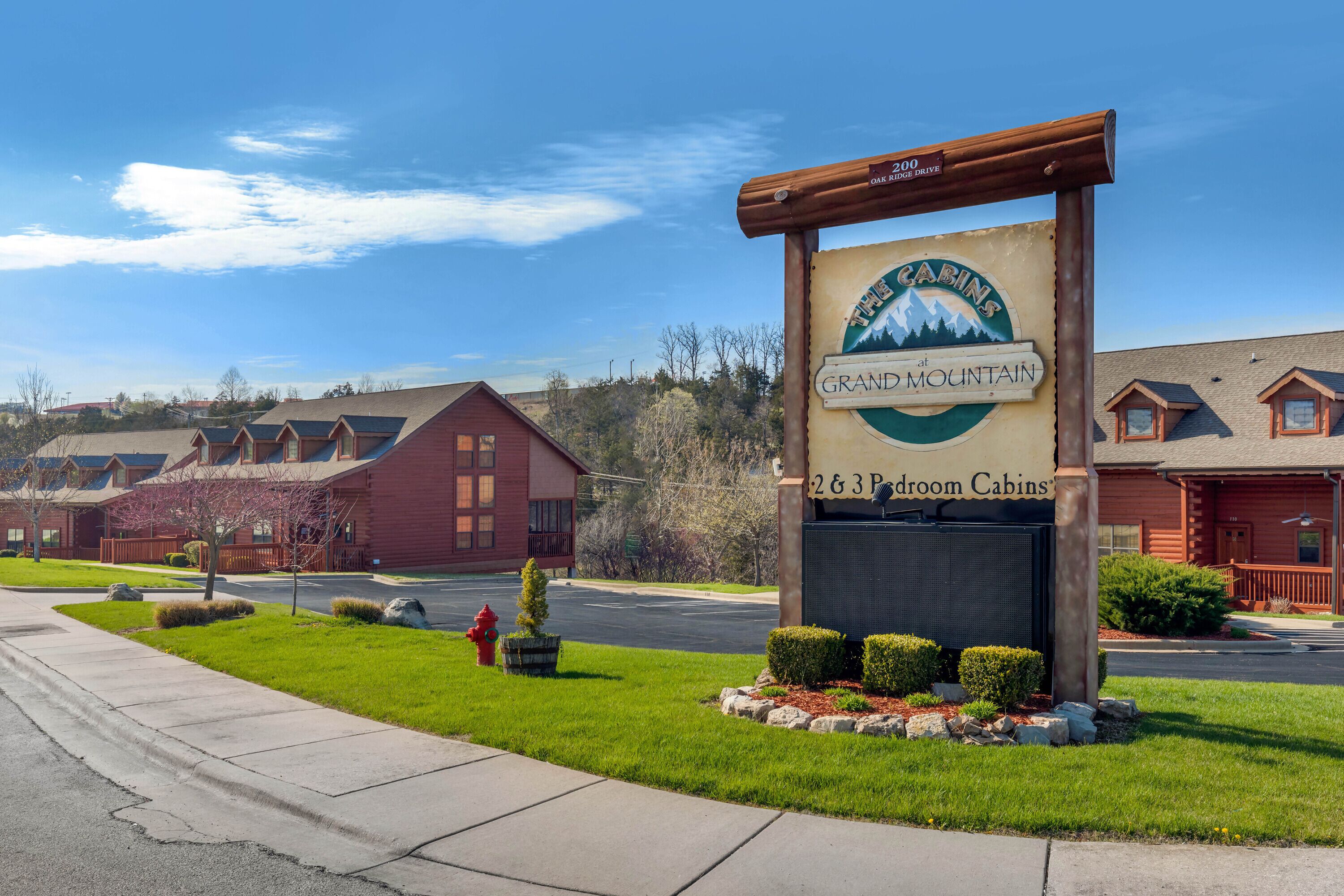 A sign for "Grand Mountain 2&3 Bedroom Cabins" with a view of the cabins and surrounding greenery.