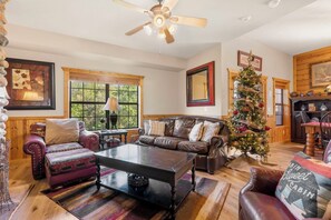 A cozy cabin interior with a leather sofa, a coffee table, a Christmas tree, and a fireplace.