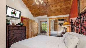 Une chambre avec un plafond en bois, un lit avec une literie blanche, une commode, un téléviseur et une fenêtre avec des stores.