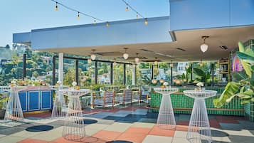 An outdoor seating area with tables and chairs, string lights, and a view of the city.