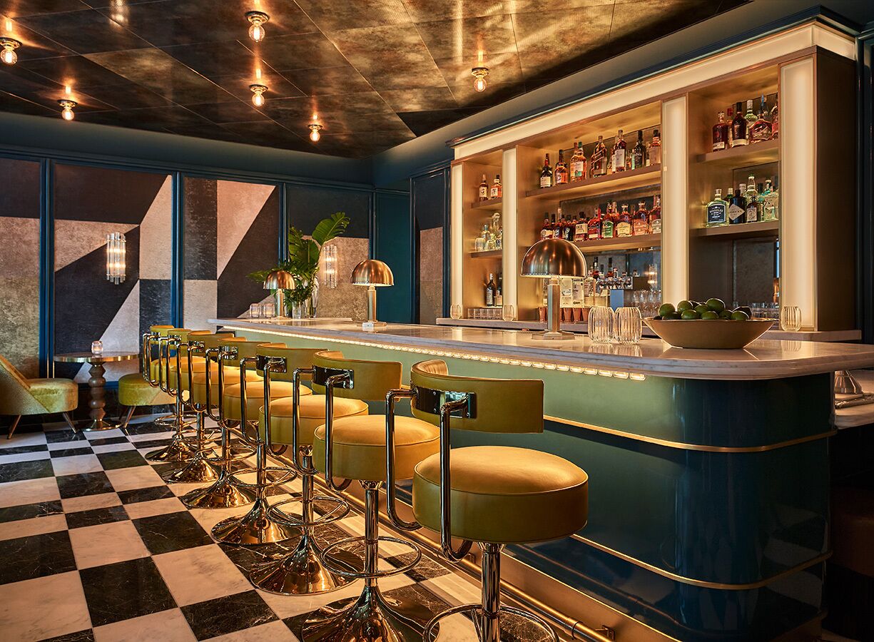 A bar area with a checkered floor, bar stools, and shelves of liquor bottles.