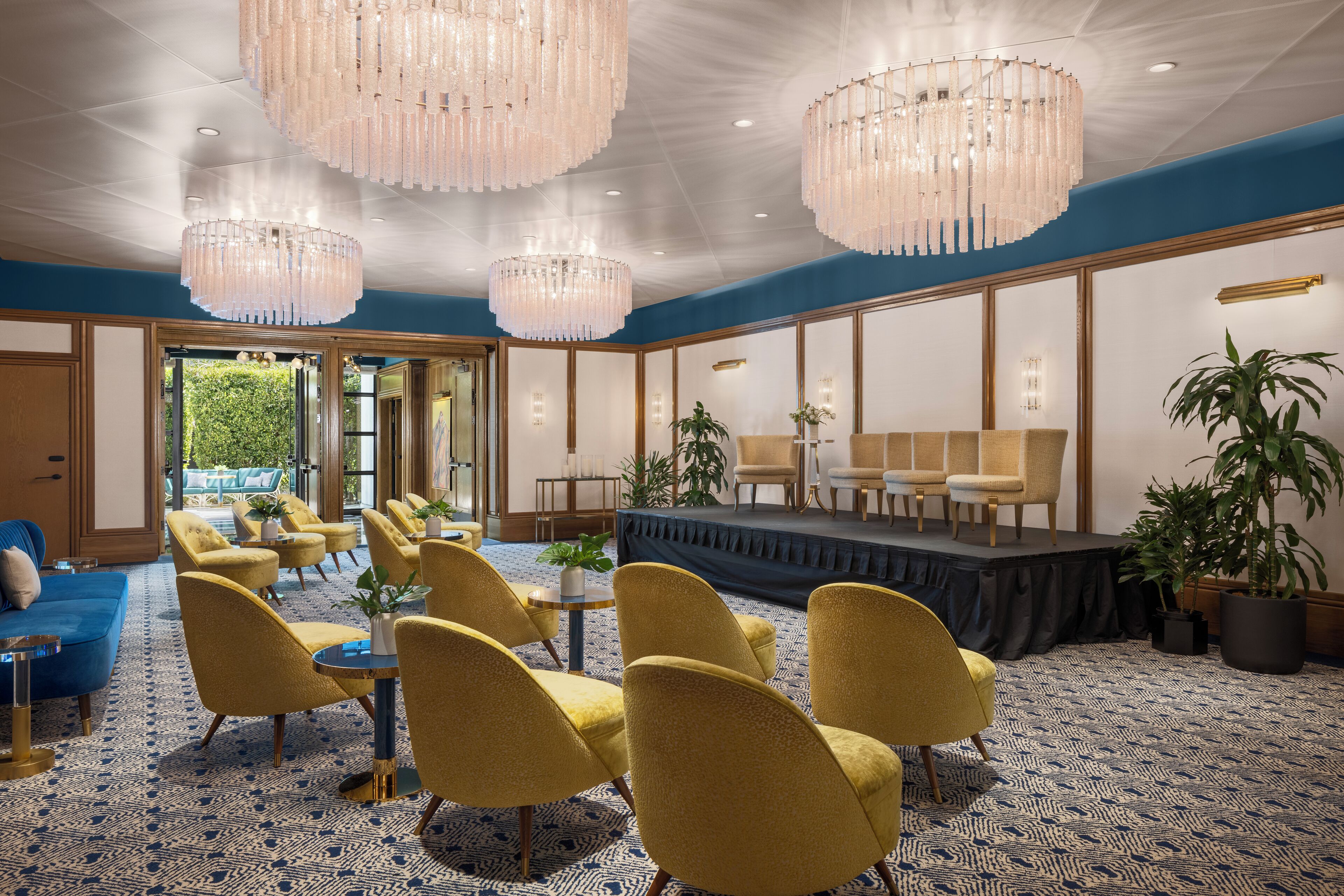 A spacious room with yellow chairs, a stage, and large chandeliers.