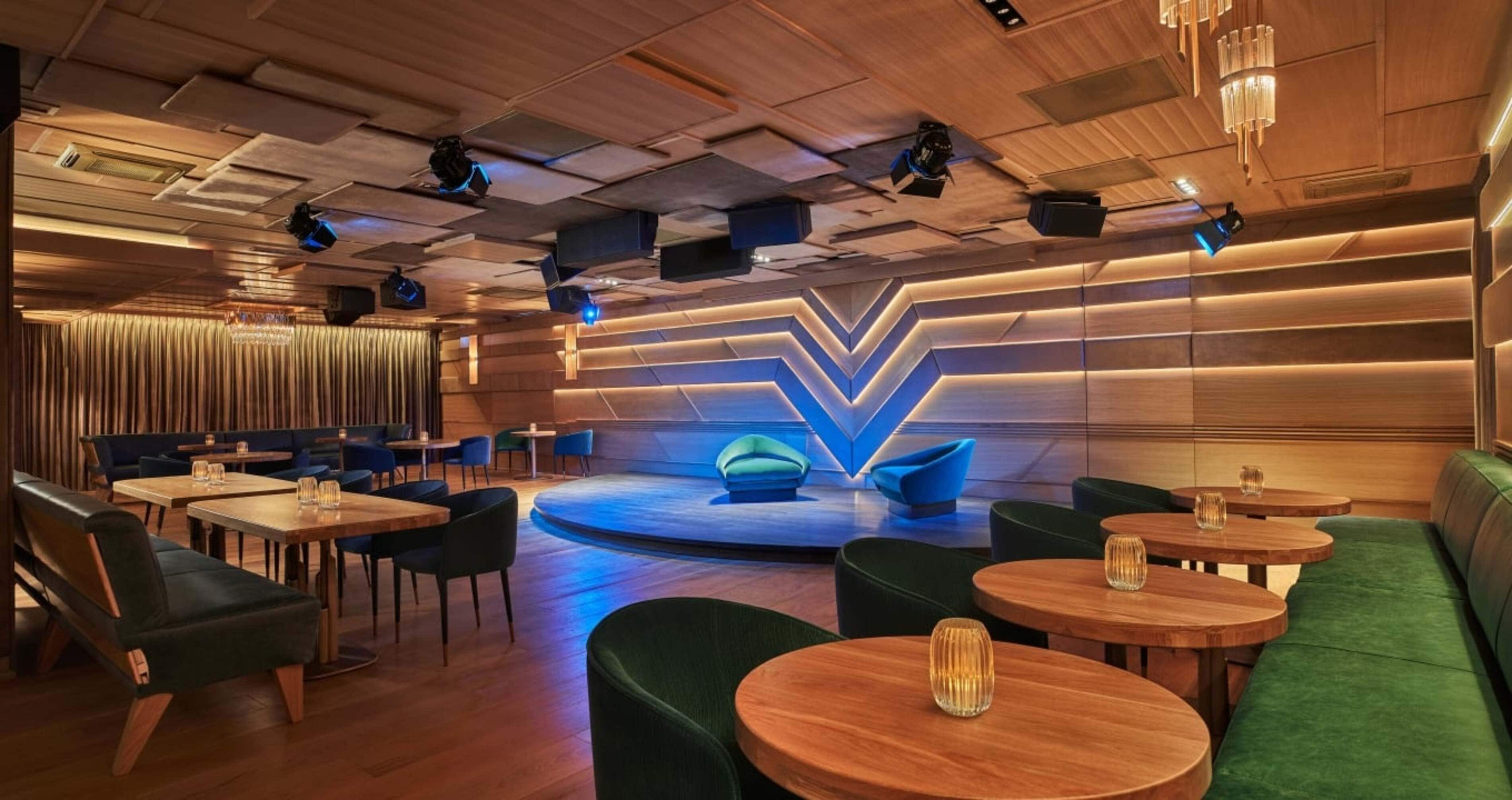 A modern lounge with a stage, green seating, and wooden tables.