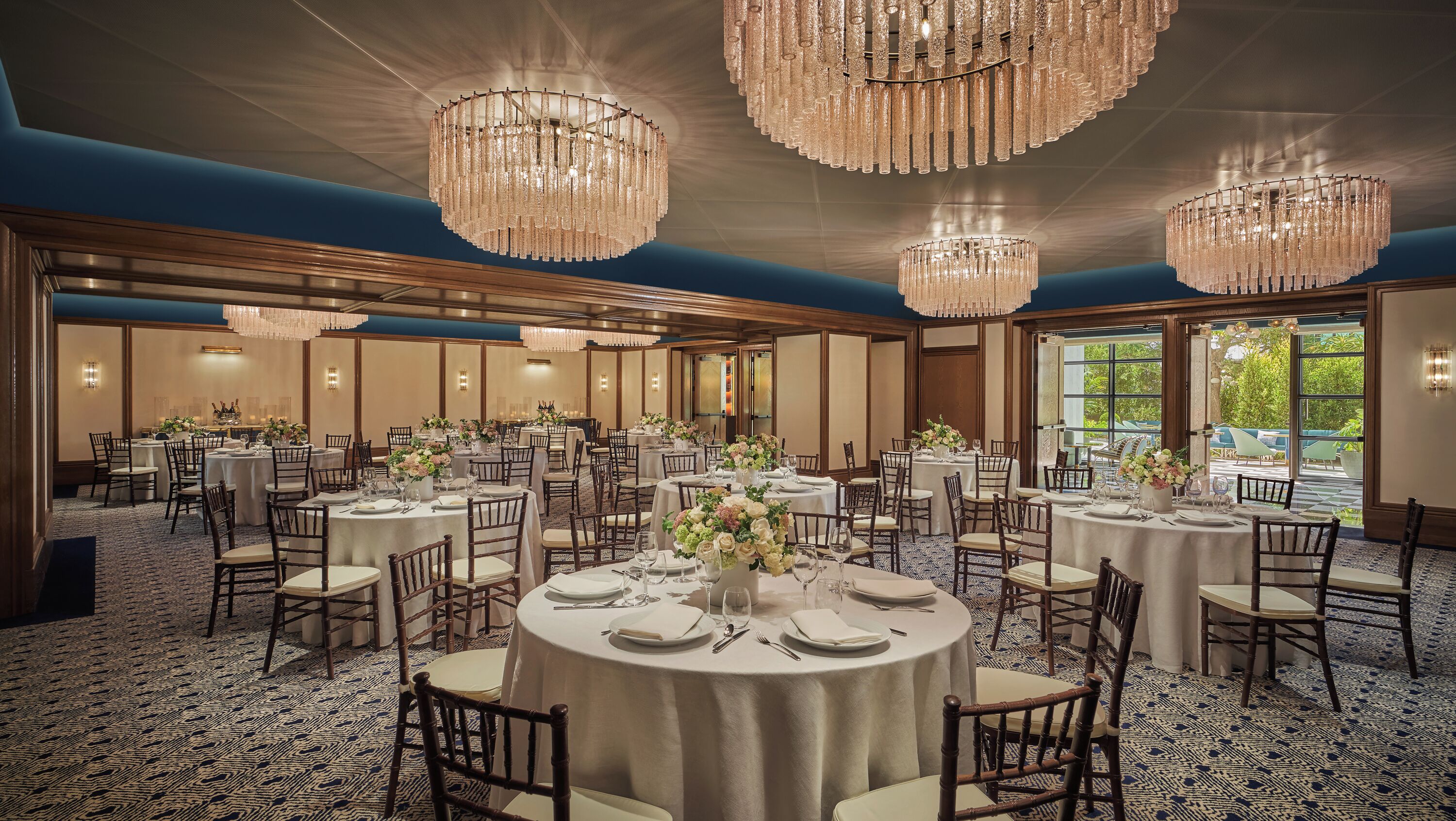 A banquet hall with round tables, chandeliers, and a patterned carpet.