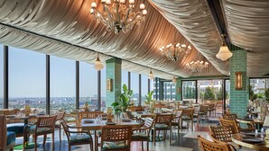 Un restaurante espacioso con techos altos, elegantes candelabros y grandes ventanales con vistas a la ciudad.