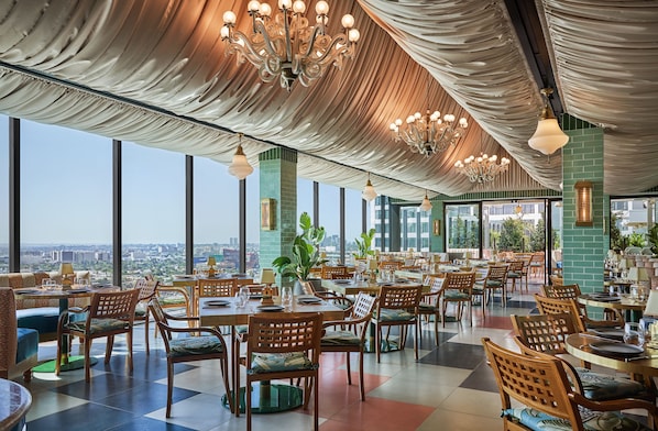 Un restaurante espacioso con techos altos, elegantes candelabros y grandes ventanales con vistas a la ciudad.