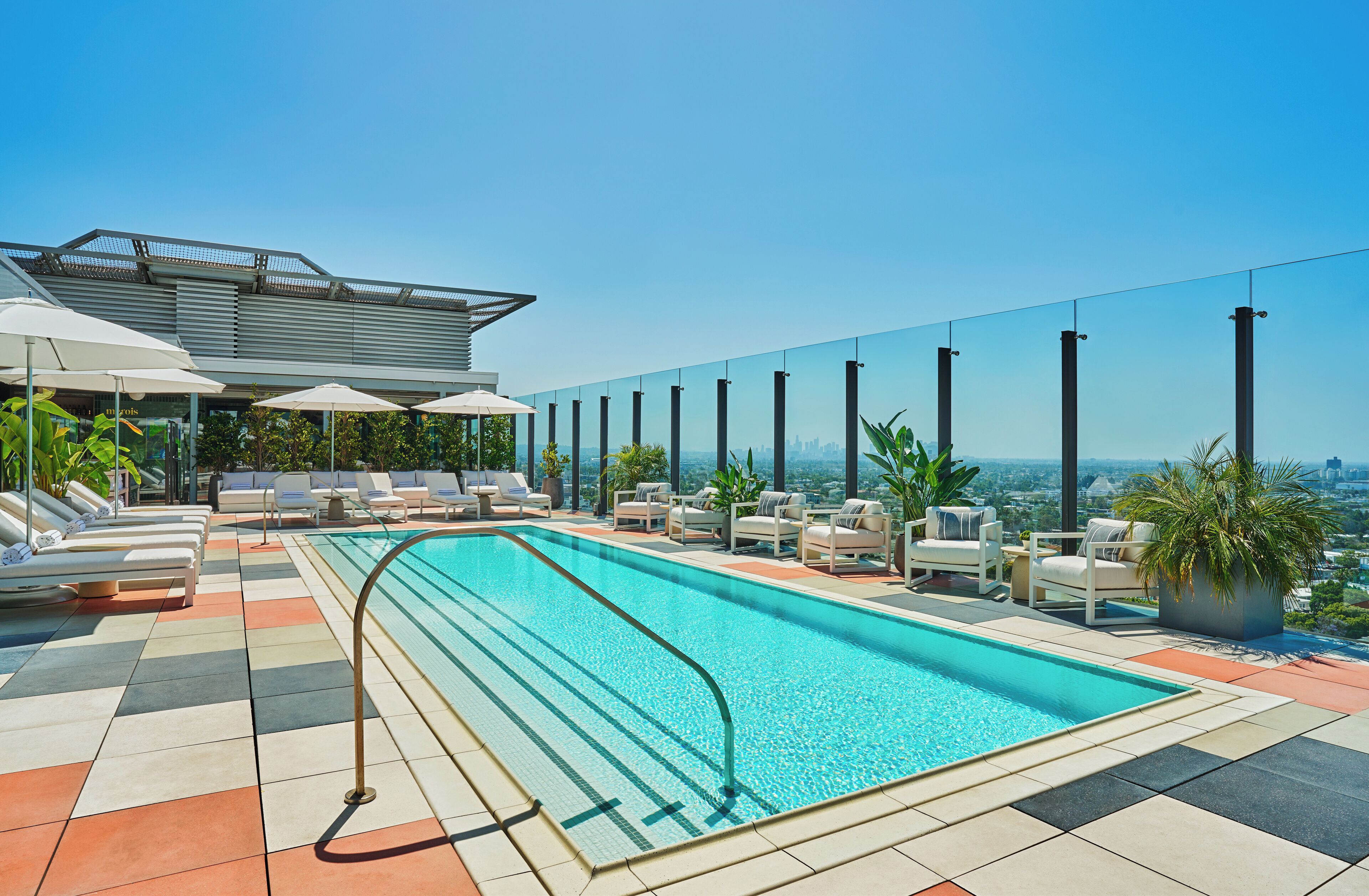 A rooftop pool with lounge chairs and umbrellas, surrounded by a city view.