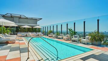 A rooftop pool with lounge chairs and umbrellas, surrounded by a city view.