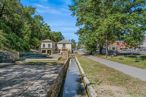 A canal with a stone wall on one side and a paved walkway on the other, leading to a building with a balcony.
