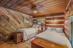 A cabin-style bedroom with two beds, a ceiling fan, and a wooden floor.