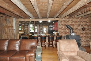 A rustic interior with wooden beams, a brick wall, a fireplace, leather sofas, and a bar area.