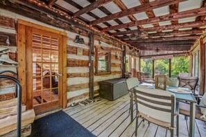 A log cabin with a porch, wooden flooring, a dining table with chairs, and a bench.