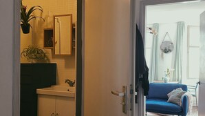 Een open doorgang naar een keuken met kasten en een aanrecht, een blauwe bank in een woonruimte, en een kleine plant op het aanrecht.