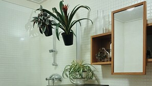 Een badkamer met witte betegelde wanden, een zwarte wastafel, een witte wasbak en twee potplanten.