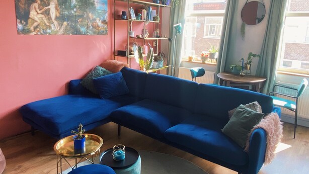 Een woonkamer met een blauwe hoekbank, een ronde salontafel en een boekenkast.