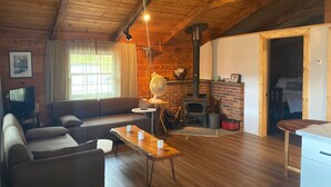 Un interior acogedor de cabaña con techo de madera, chimenea de ladrillo, sofá, mesa y televisor.
