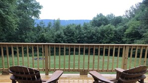 Una terraza de madera con dos sillas Adirondack mirando hacia un jardín y árboles.
