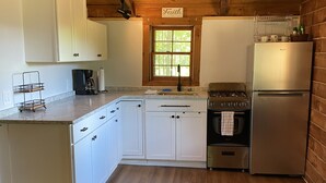 Una cocina con armarios blancos, un refrigerador de acero inoxidable, una estufa a gas y una ventana con vista a árboles.