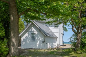 A white two-story house with a gabled roof, surrounded by trees and a beach view.