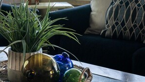 Una habitación con vista a la playa, un sofá azul oscuro, una lámpara y una cesta con adornos.