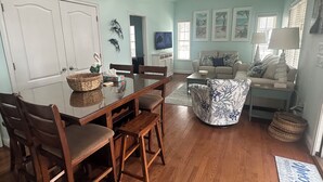Un área de comedor con una mesa y sillas de madera, un sofá y una televisión al fondo.