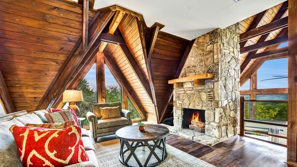 Una habitación acogedora con chimenea de piedra, vigas de madera y un amplio ventanal con vistas panorámicas.