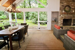 An outdoor patio with a wooden table and chairs, a wicker sofa, and a fireplace. - Idlewood Cottage: Cozy Home w/ Covered Porch, Firepit, Yard | 8 Min to Downtown (Highlands)