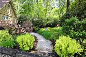 A house with a garden path leading to a wooden deck, surrounded by lush greenery. - Idlewood Cottage: Cozy Home w/ Covered Porch, Firepit, Yard | 8 Min to Downtown (Highlands)