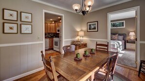 A dining area with a wooden table and chairs, framed pictures on the wall, and a chandelier. - Idlewood Cottage: Cozy Home w/ Covered Porch, Firepit, Yard | 8 Min to Downtown (Highlands)