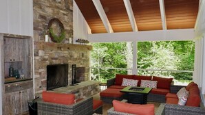 A cozy living room with a stone fireplace, wicker furniture, and a large window overlooking greenery. - Idlewood Cottage: Cozy Home w/ Covered Porch, Firepit, Yard | 8 Min to Downtown (Highlands)