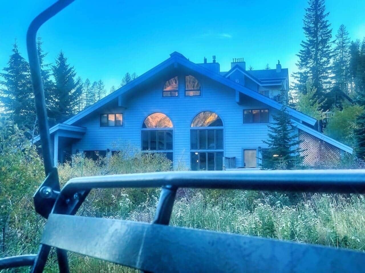 A blue house with a gabled roof and large windows, surrounded by trees.
