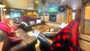 A spacious living room with a stone fireplace, leather sofas, and a wooden coffee table. - True Slopeside 7-Bedroom Home: 75ft to Chair, Private Hot Tub, Deck, Sleeps 16 (Whitefish)