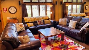 A cozy living room with leather sofas, a coffee table, and a large window providing a view of the outdoors. - True Slopeside 7-Bedroom Home: 75ft to Chair, Private Hot Tub, Deck, Sleeps 16 (Whitefish)