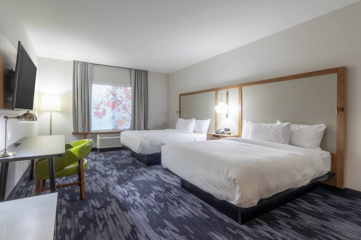 A hotel room with two beds, a desk, a chair, a TV, and a window with curtains.
