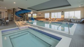 Une grande piscine intérieure dotée d’un toboggan bleu, de plusieurs couloirs de nage et d’un espace ensoleillé avec des chaises.