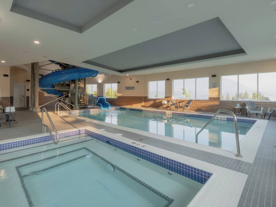 A large indoor swimming pool with a blue slide, multiple lanes, and a sunlit area with chairs.