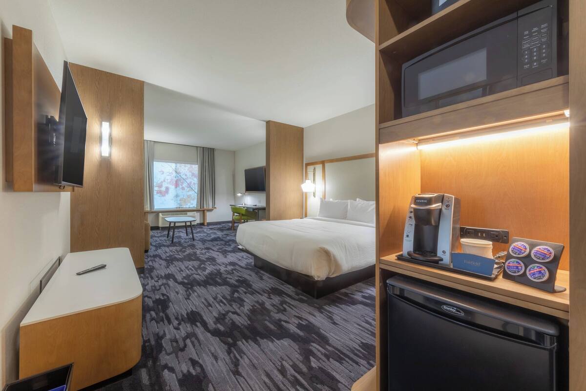 A hotel room with a bed, a desk, a microwave, a coffee maker, and a small refrigerator.