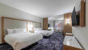 Une chambre d’hôtel avec deux lits, un bureau, une chaise, un téléviseur à écran plat et une grande fenêtre avec des rideaux.