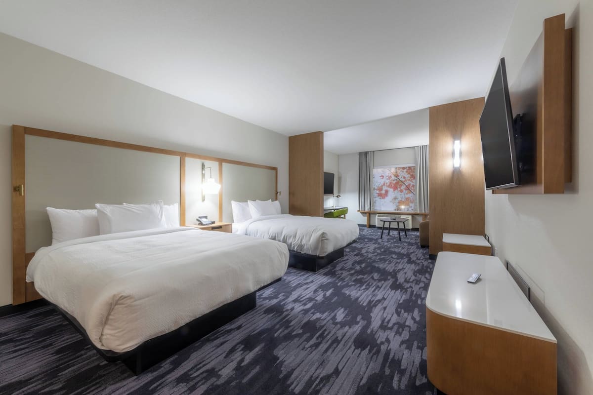 A hotel room with two beds, a desk, a chair, a flat-screen TV, and a large window with curtains.