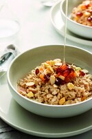 Un tazón de avena con nueces y frutas secas, siendo rociado con miel.